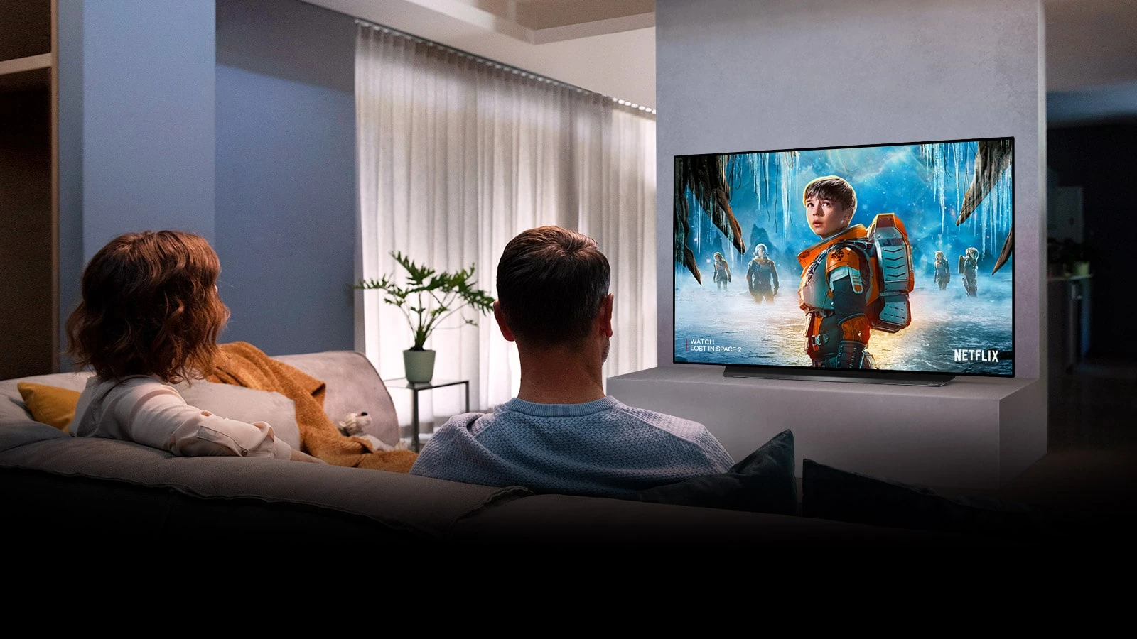 Couple assis sur un canapé dans le salon en regardant un film romantique à la télé